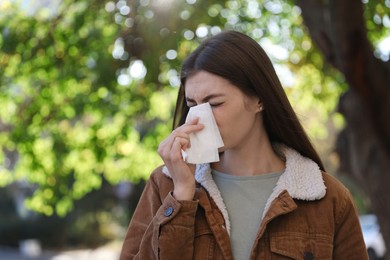 Woman with runny nose in park, space for text