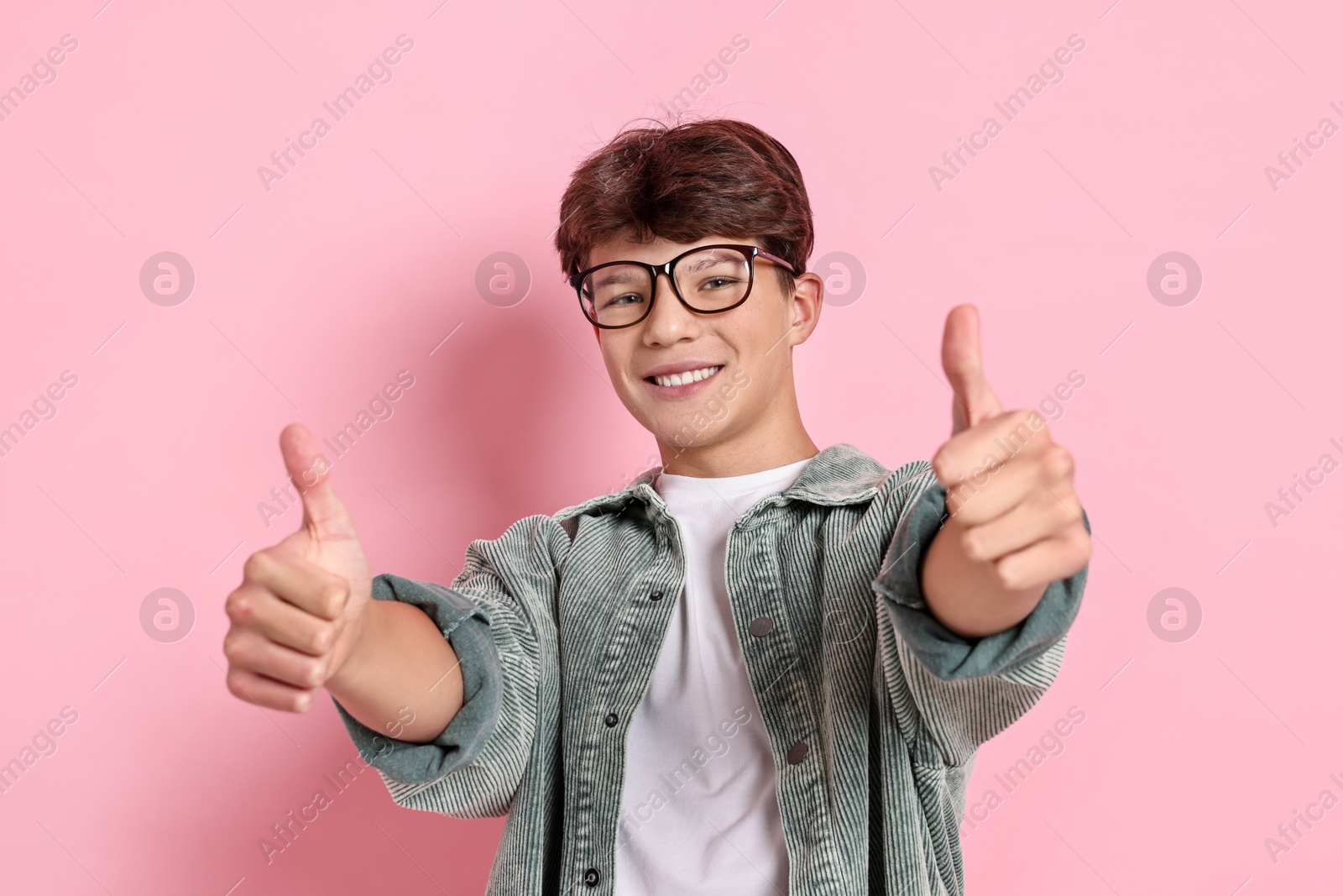 Photo of Happy teenage boy showing thumbs up on pink background