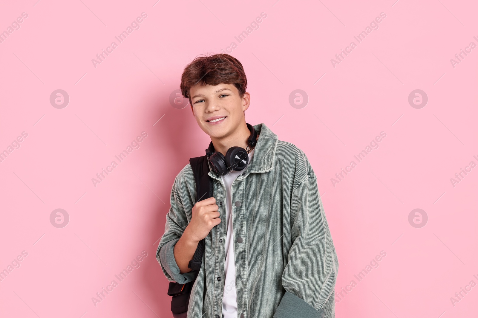 Photo of Happy teenage boy with headphones and backpack on pink background