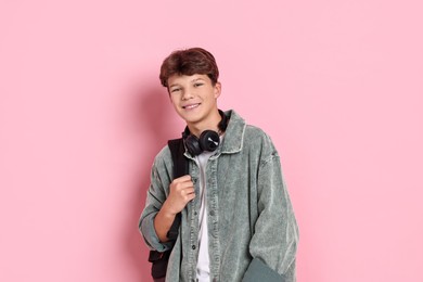 Photo of Happy teenage boy with headphones and backpack on pink background