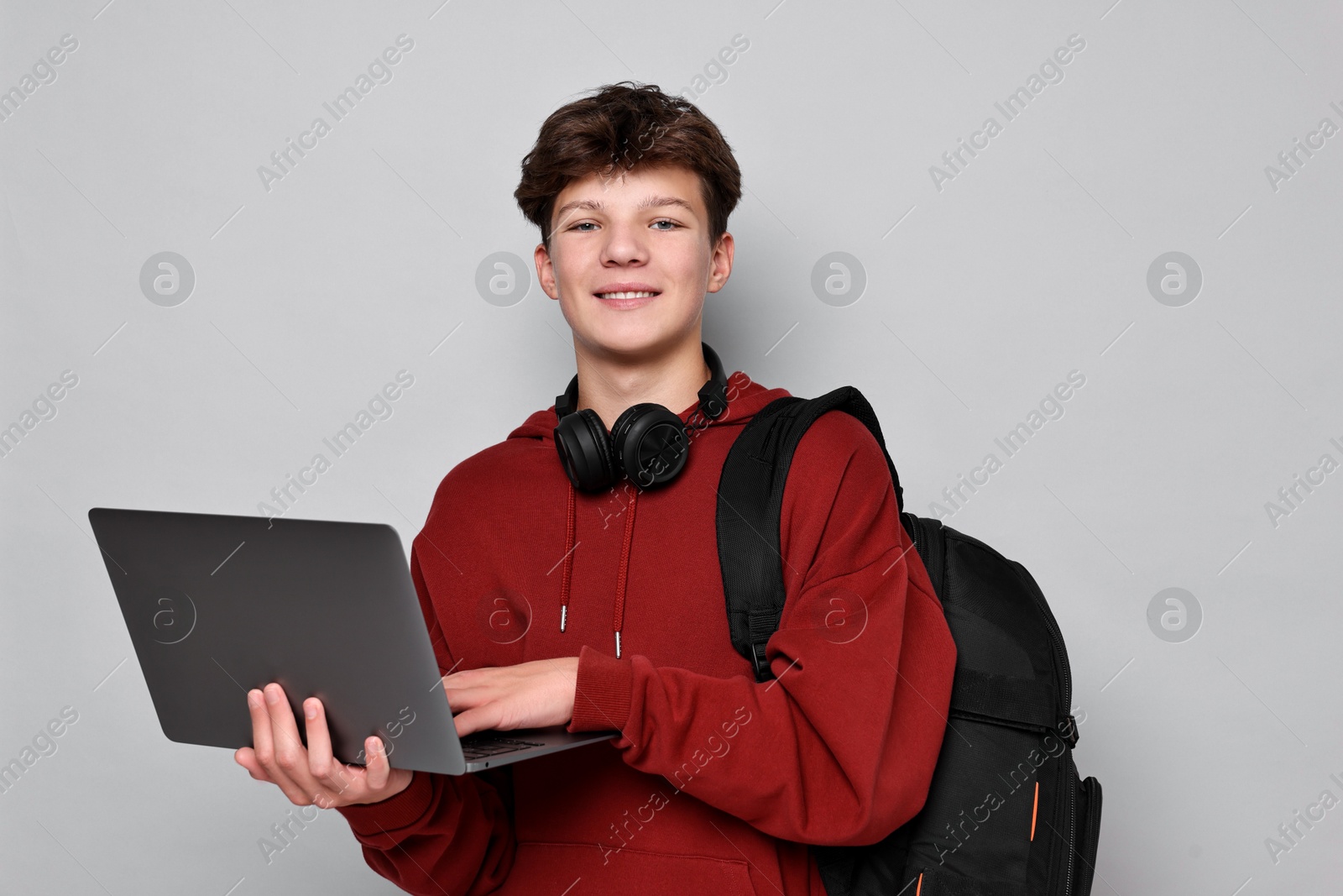 Photo of Teenage boy with headphones, laptop and backpack on light grey background