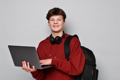 Photo of Teenage boy with headphones, laptop and backpack on light grey background