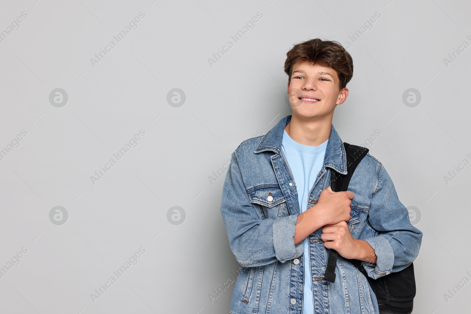 Photo of Happy teenage boy with backpack on light grey background, space for text