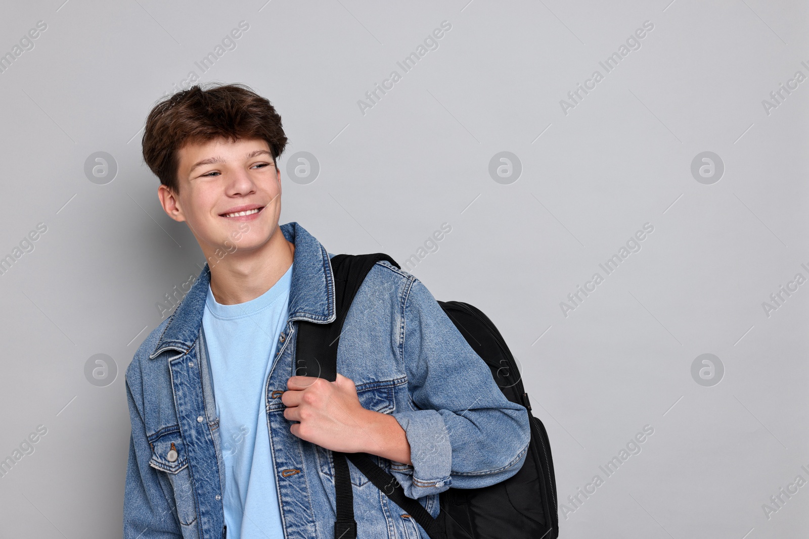 Photo of Happy teenage boy with backpack on light grey background, space for text