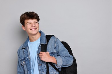 Photo of Happy teenage boy with backpack on light grey background, space for text