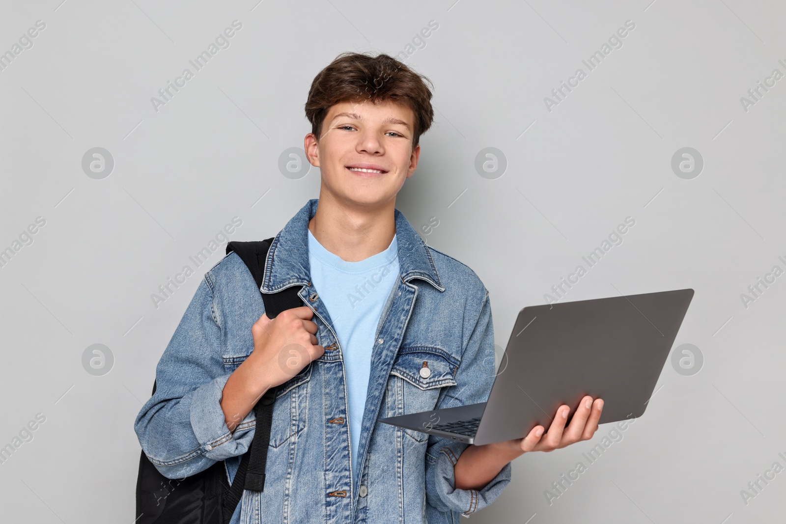 Photo of Happy teenage boy with laptop and backpack on light grey background