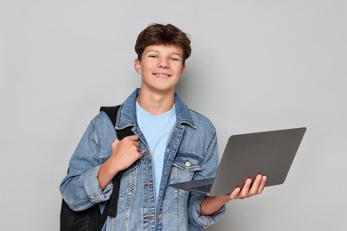 Photo of Happy teenage boy with laptop and backpack on light grey background