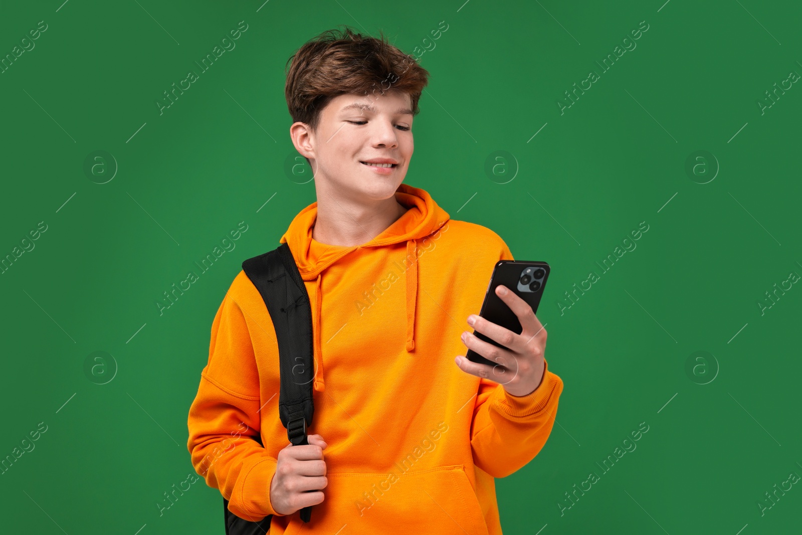 Photo of Teenage boy with smartphone and backpack on green background