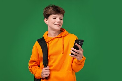 Photo of Teenage boy with smartphone and backpack on green background