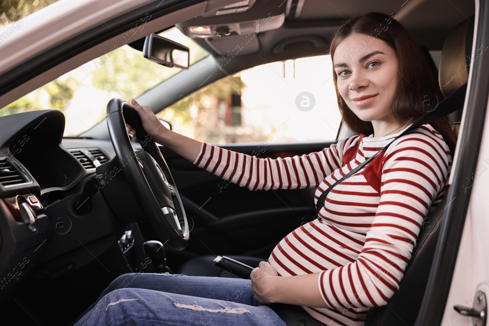 Photo of Pregnant woman with safety belt driving car, view from outside