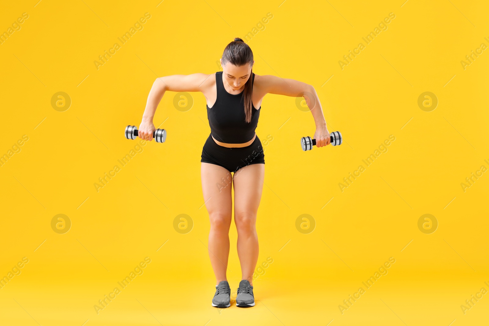 Photo of Woman exercising with dumbbells on orange background