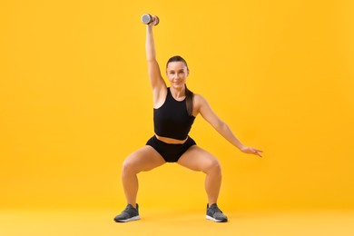 Photo of Woman exercising with dumbbell on orange background