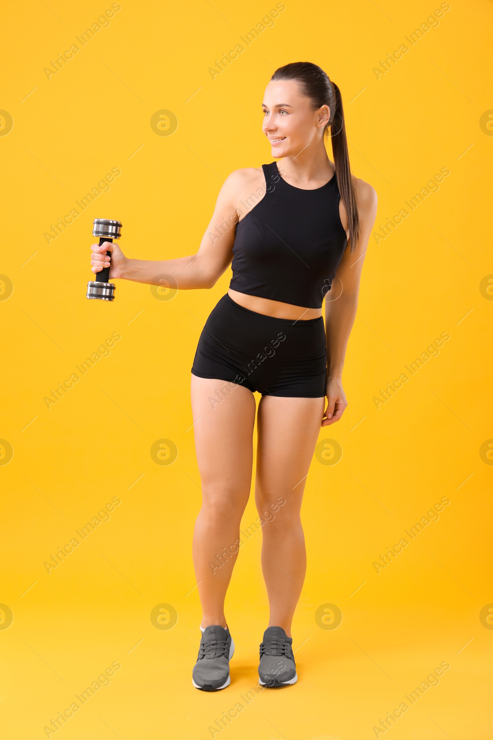 Photo of Woman exercising with dumbbell on orange background