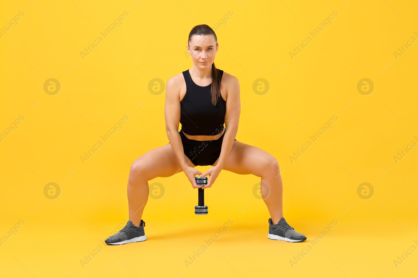 Photo of Woman exercising with dumbbell on orange background