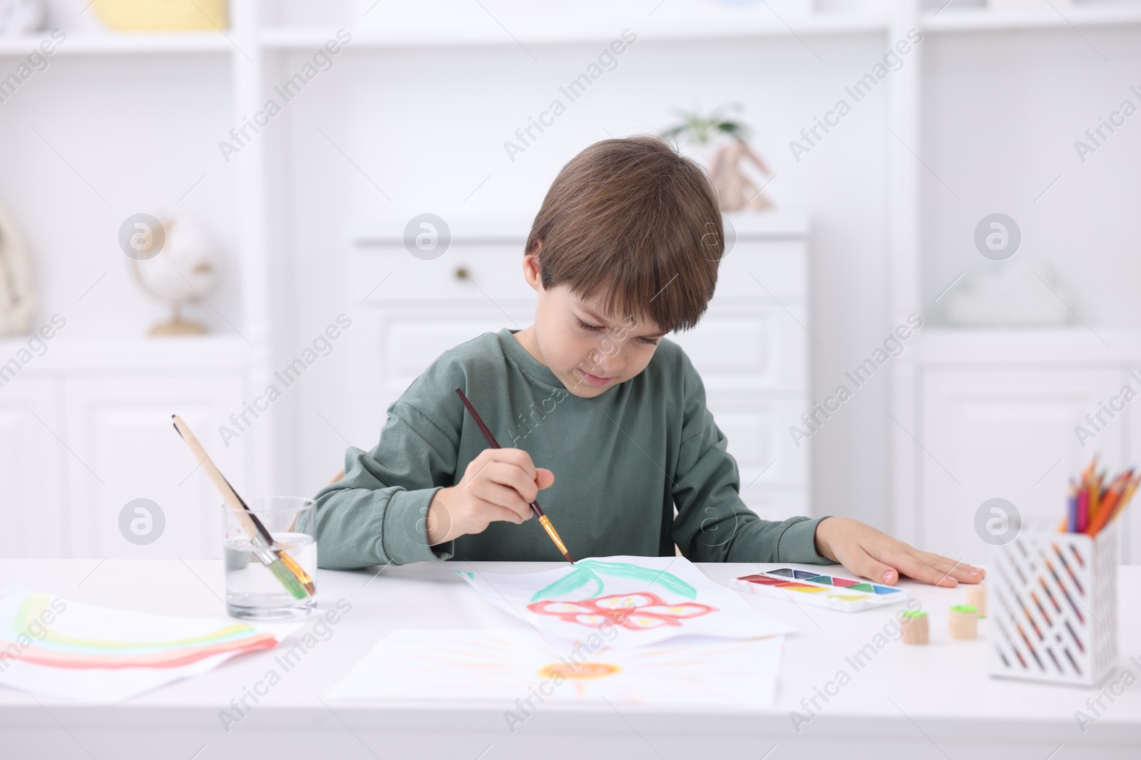 Photo of Cute boy drawing at white table in kindergarten