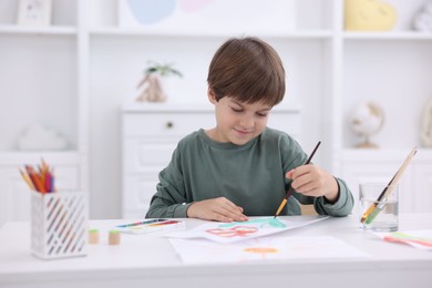 Cute boy drawing at white table in kindergarten