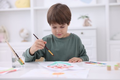 Photo of Cute boy drawing at white table in kindergarten