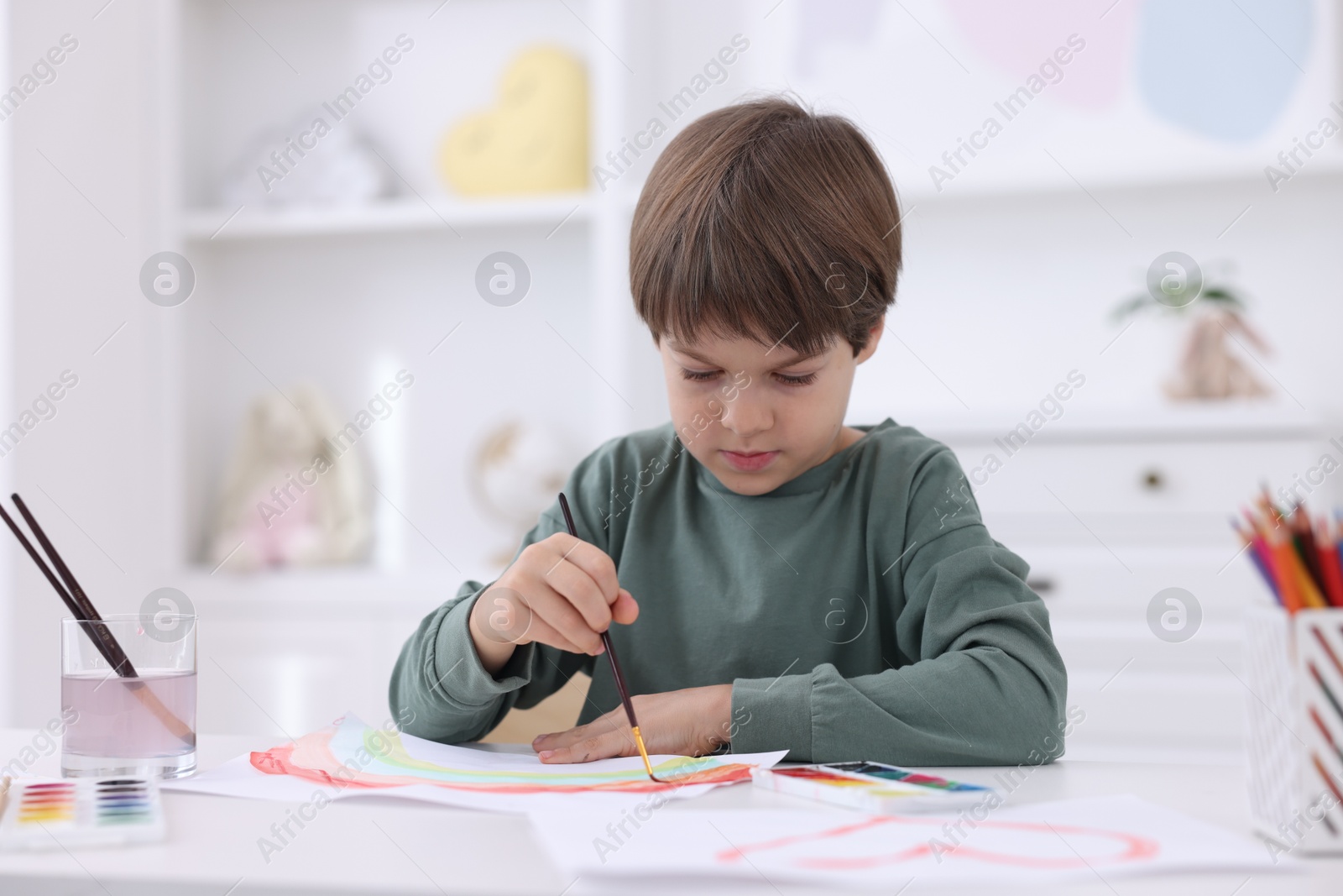 Photo of Cute boy drawing at white table in kindergarten