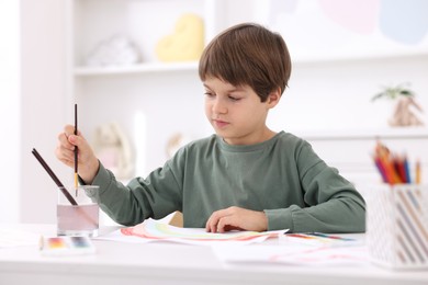 Cute boy drawing at white table in kindergarten