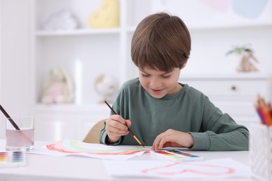 Photo of Cute boy drawing at white table in kindergarten