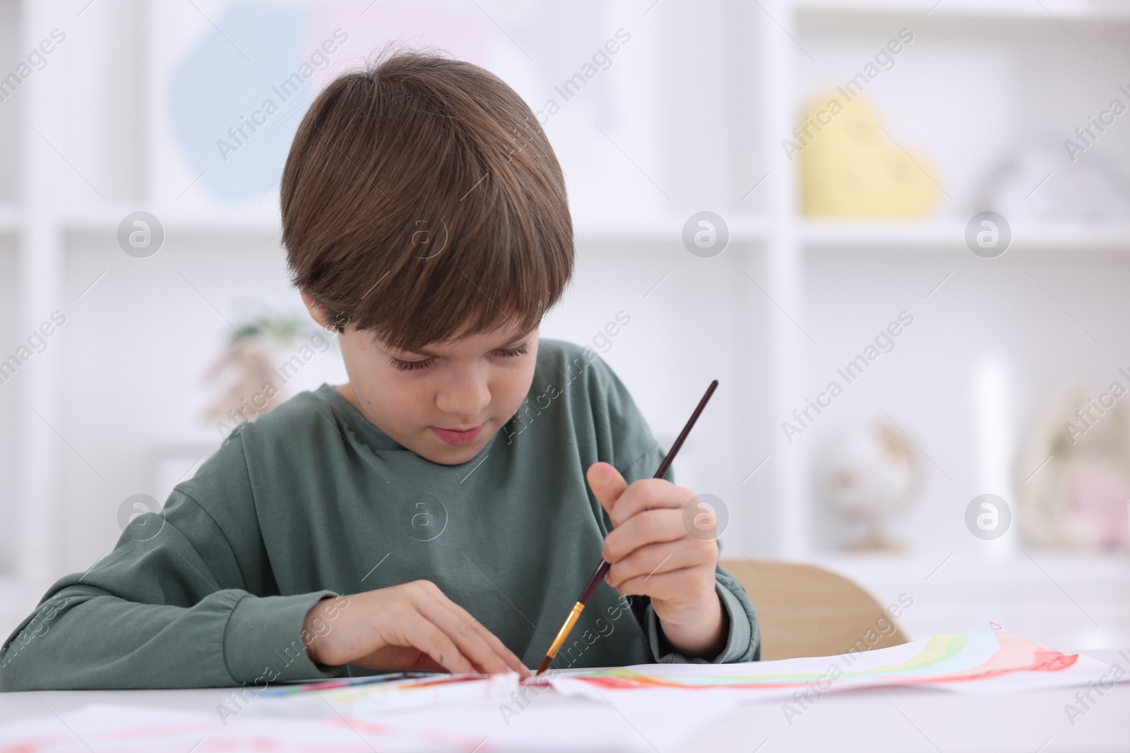 Photo of Cute boy drawing at white table in kindergarten