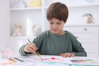 Photo of Cute boy drawing at white table in kindergarten