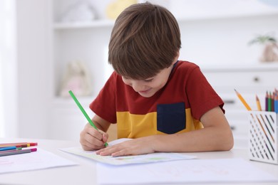 Photo of Cute boy drawing at white table in kindergarten