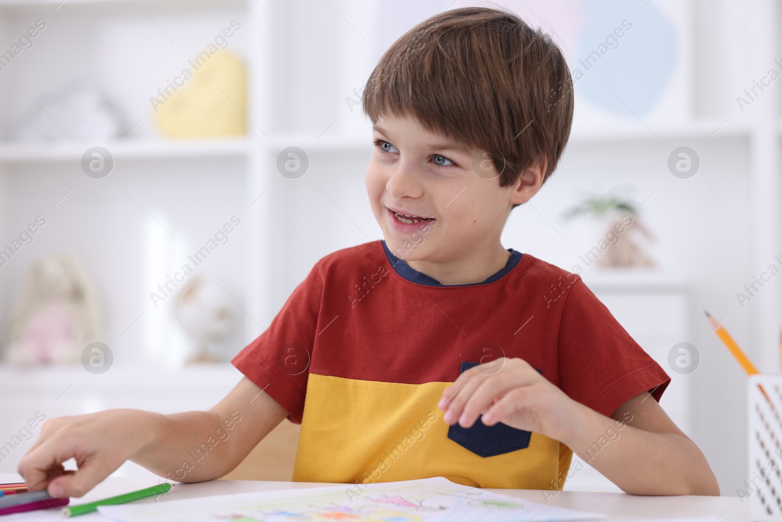 Photo of Cute boy drawing at white table in kindergarten