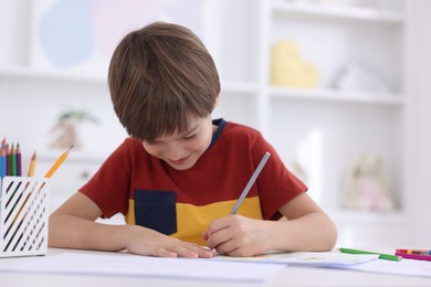 Cute boy drawing at white table in kindergarten