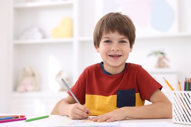 Photo of Happy boy drawing at white table in kindergarten