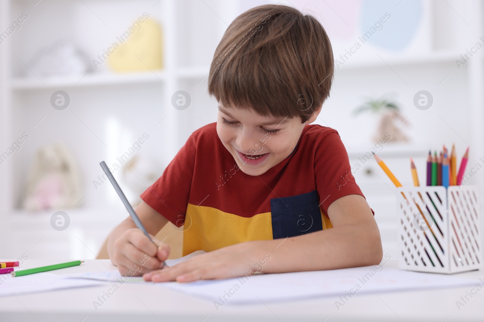 Photo of Happy boy drawing at white table in kindergarten