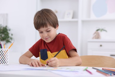 Photo of Cute boy drawing at white table in kindergarten