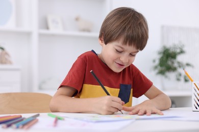 Photo of Cute boy drawing at white table in kindergarten