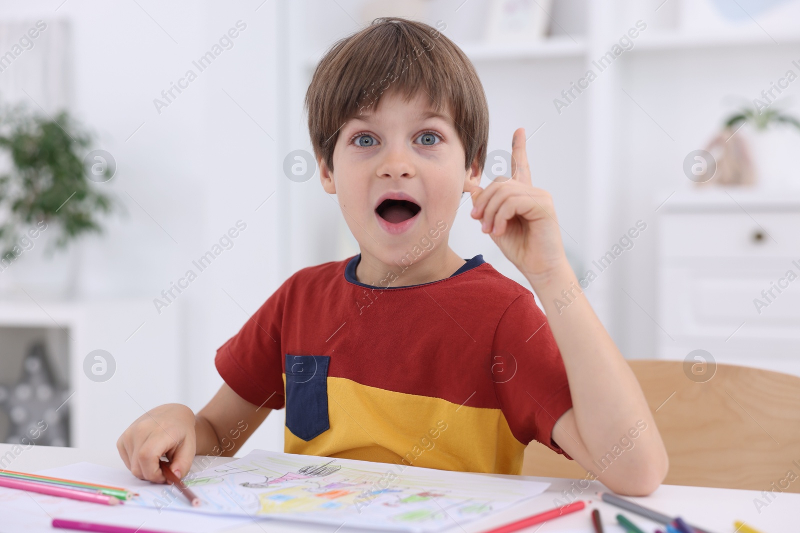 Photo of Emotional boy had idea for his drawing at white table in kindergarten