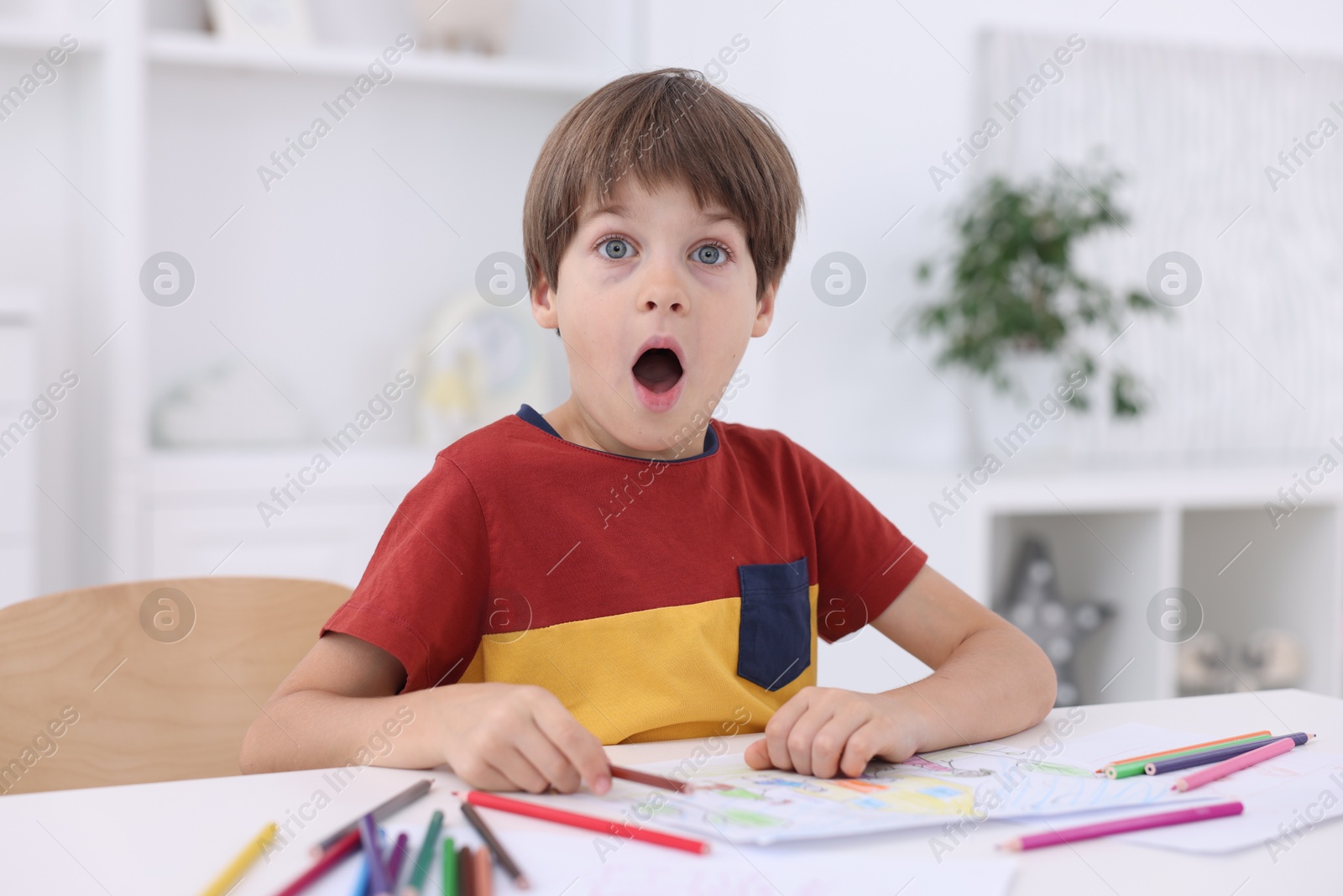 Photo of Emotional boy at white table with drawing in kindergarten