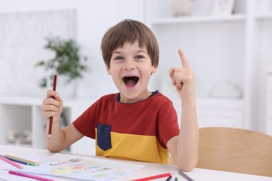 Photo of Emotional boy had idea for his drawing at white table in kindergarten