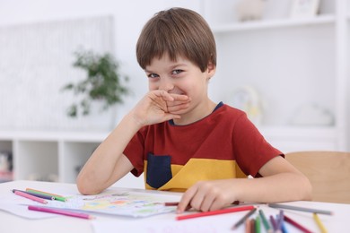 Photo of Cute boy at white table with drawing in kindergarten