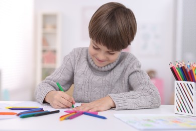 Photo of Cute boy drawing at white table in kindergarten