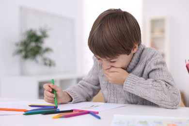 Photo of Cute boy drawing at white table in kindergarten