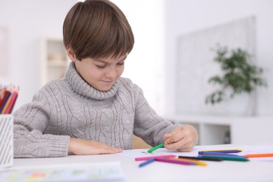 Cute boy drawing at white table in kindergarten