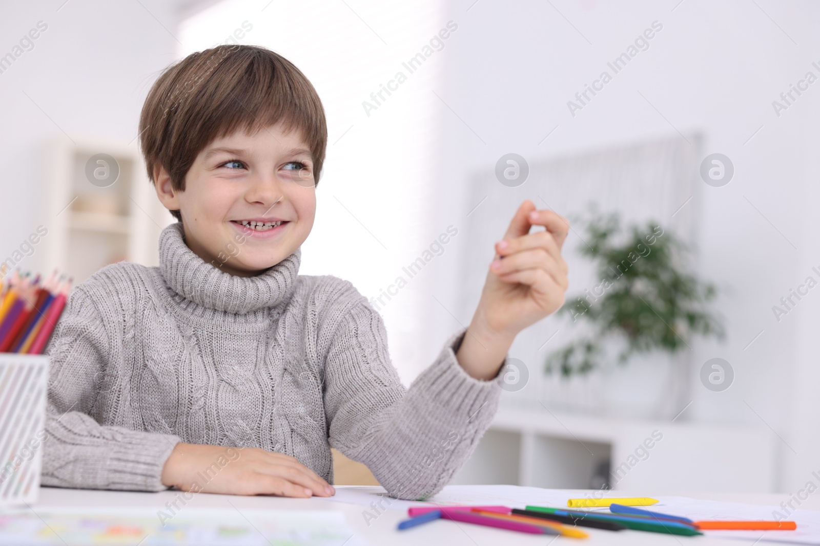 Photo of Happy boy drawing at white table in kindergarten