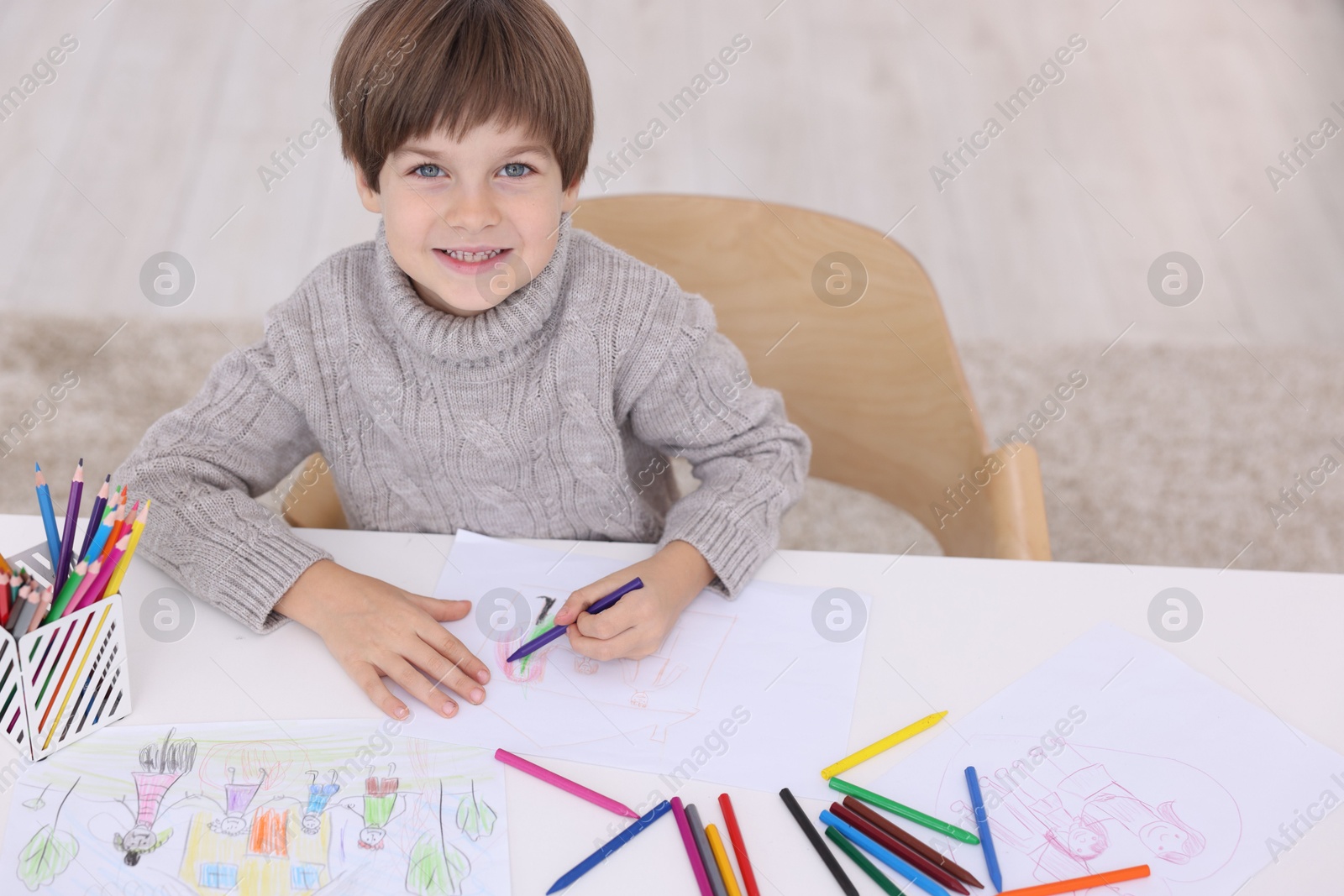 Photo of Happy boy drawing at white table indoors