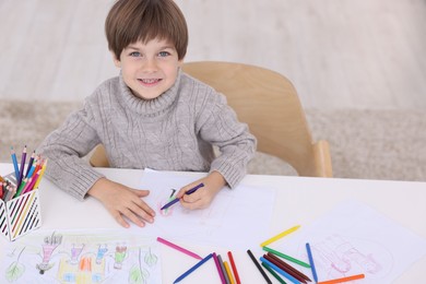 Photo of Happy boy drawing at white table indoors