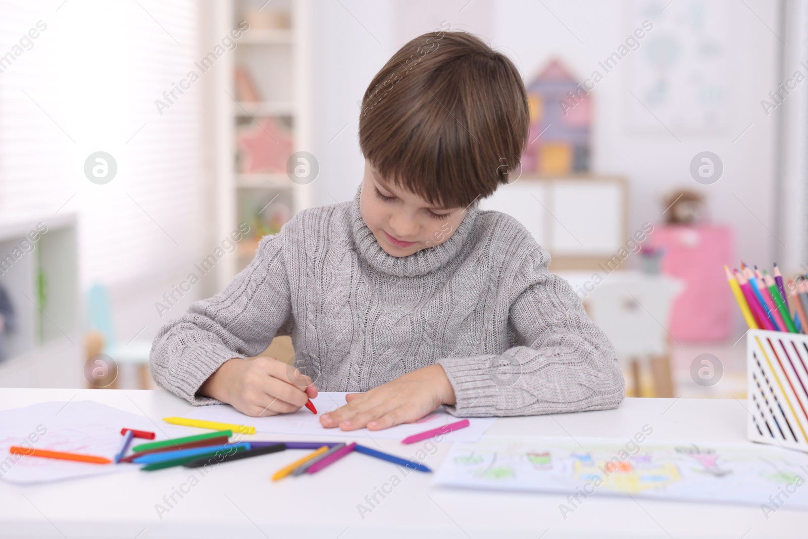 Photo of Cute boy drawing at white table in kindergarten