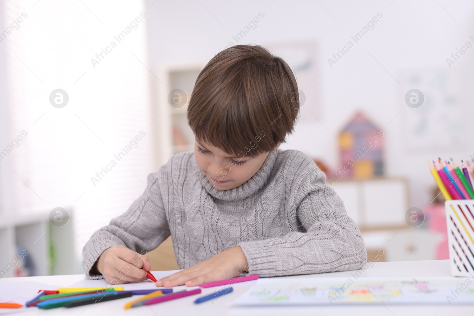 Photo of Cute boy drawing at white table in kindergarten