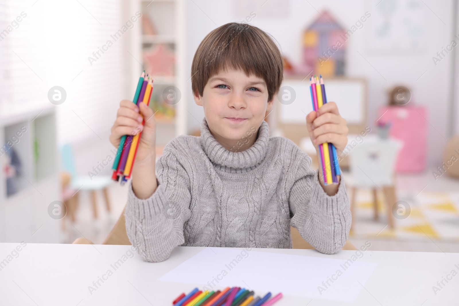 Photo of Portrait of cute boy with colorful pencils at white table in kindergarten