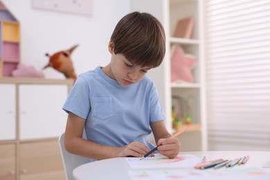 Photo of Cute boy drawing at white table in kindergarten