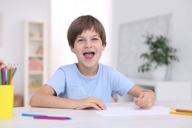 Funny boy drawing at white table in kindergarten