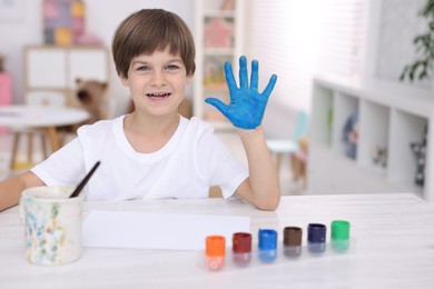 Happy boy drawing with palm at light wooden table in kindergarten