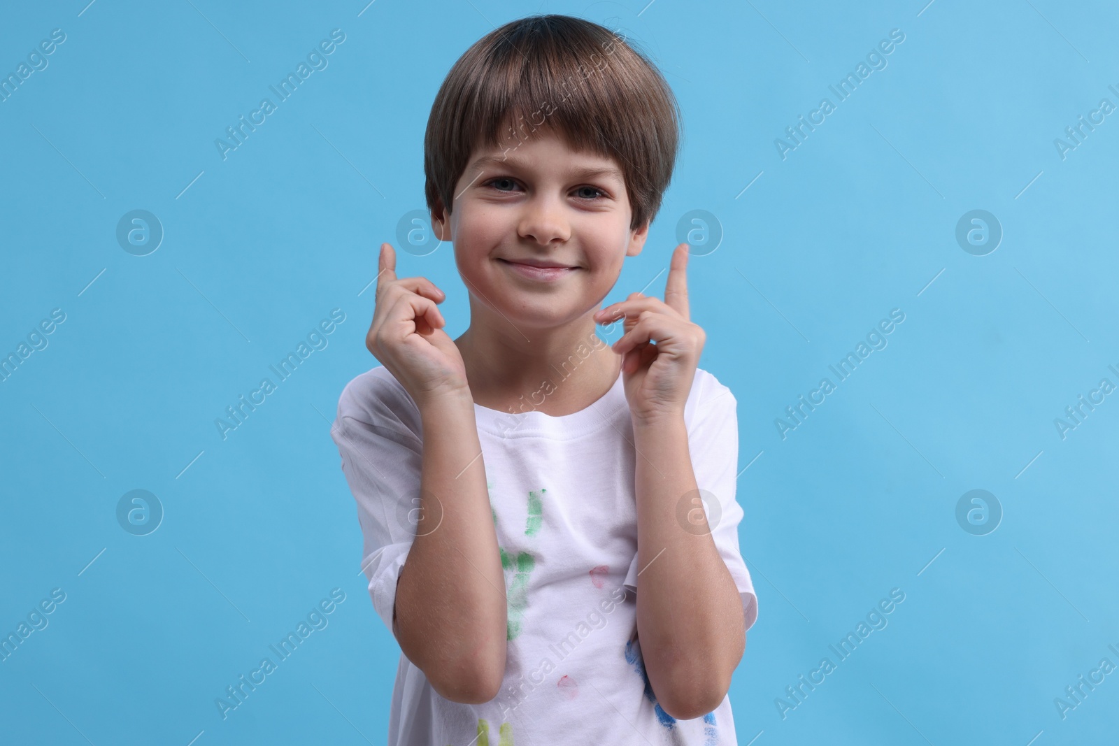 Photo of Portrait of cute boy in t-shirt with handprints drawings on light blue background